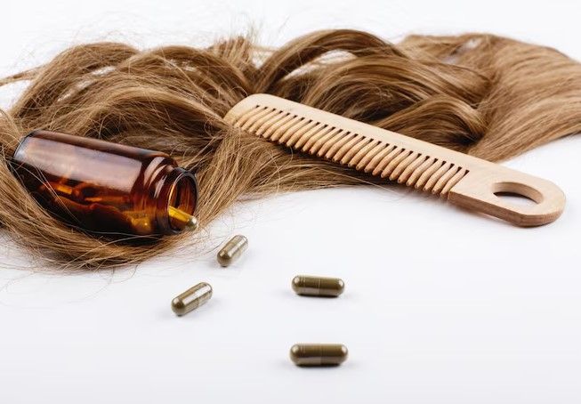 Holzkamm und Flasche mit Vitaminen liegen auf braunen Haarlocken